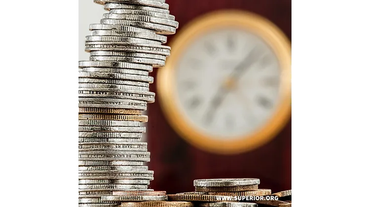Tall stack of coins with a blurt clock in the background - Time and money