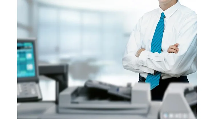 Man in blue tie standing at printer in business office